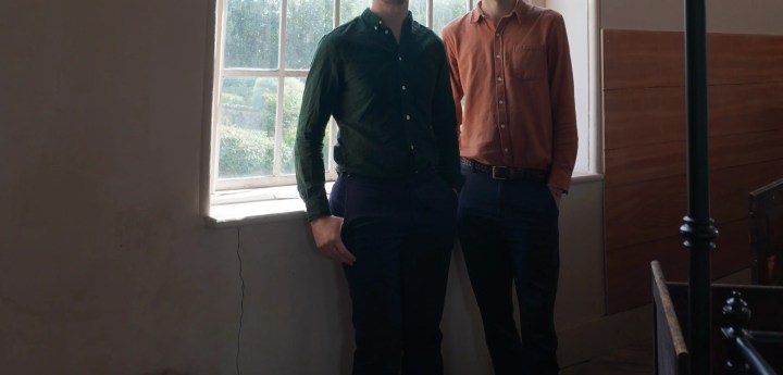 Two people standing in front of a metal window with antique stage light